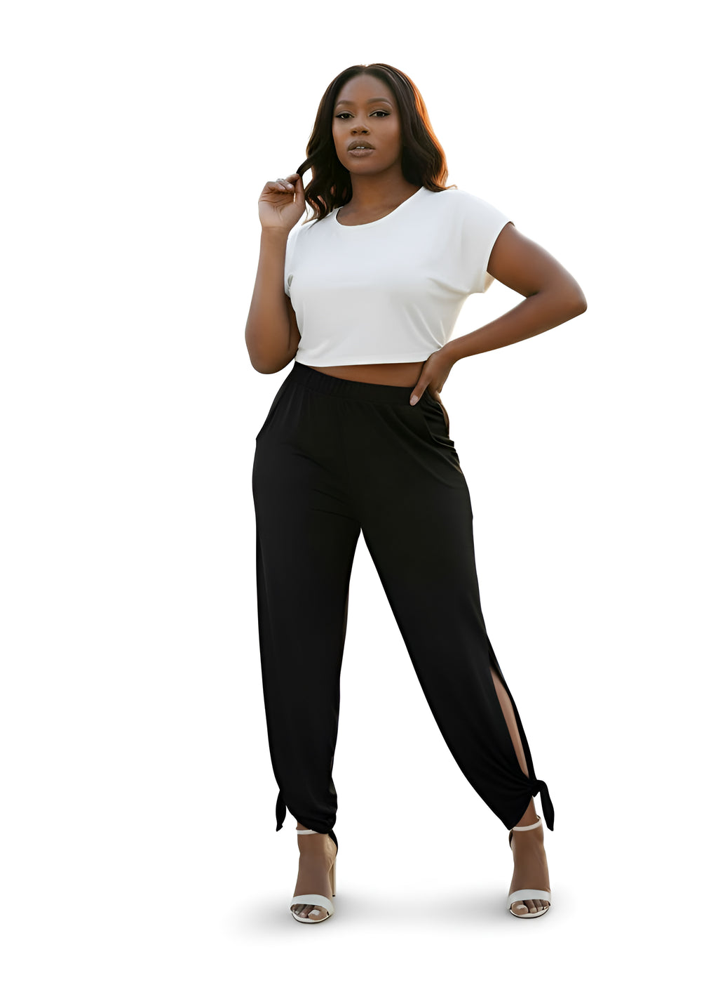 Woman wearing a white crop top and black pants with a side slit on a white background
