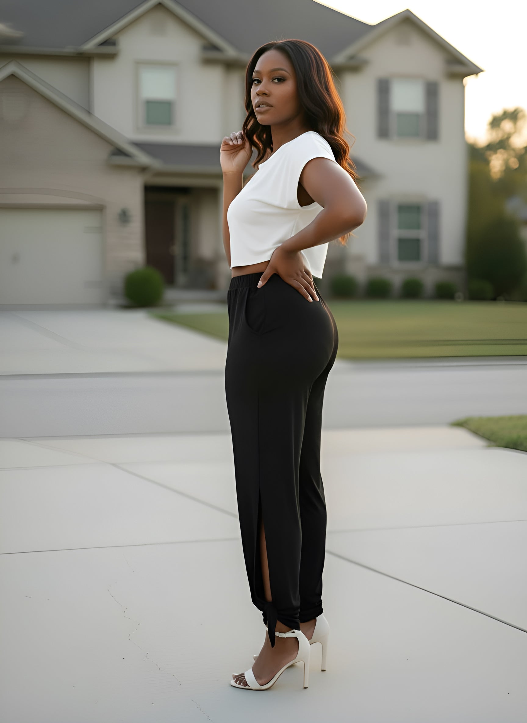 Woman in a white top and black pants standing in front of a house.
