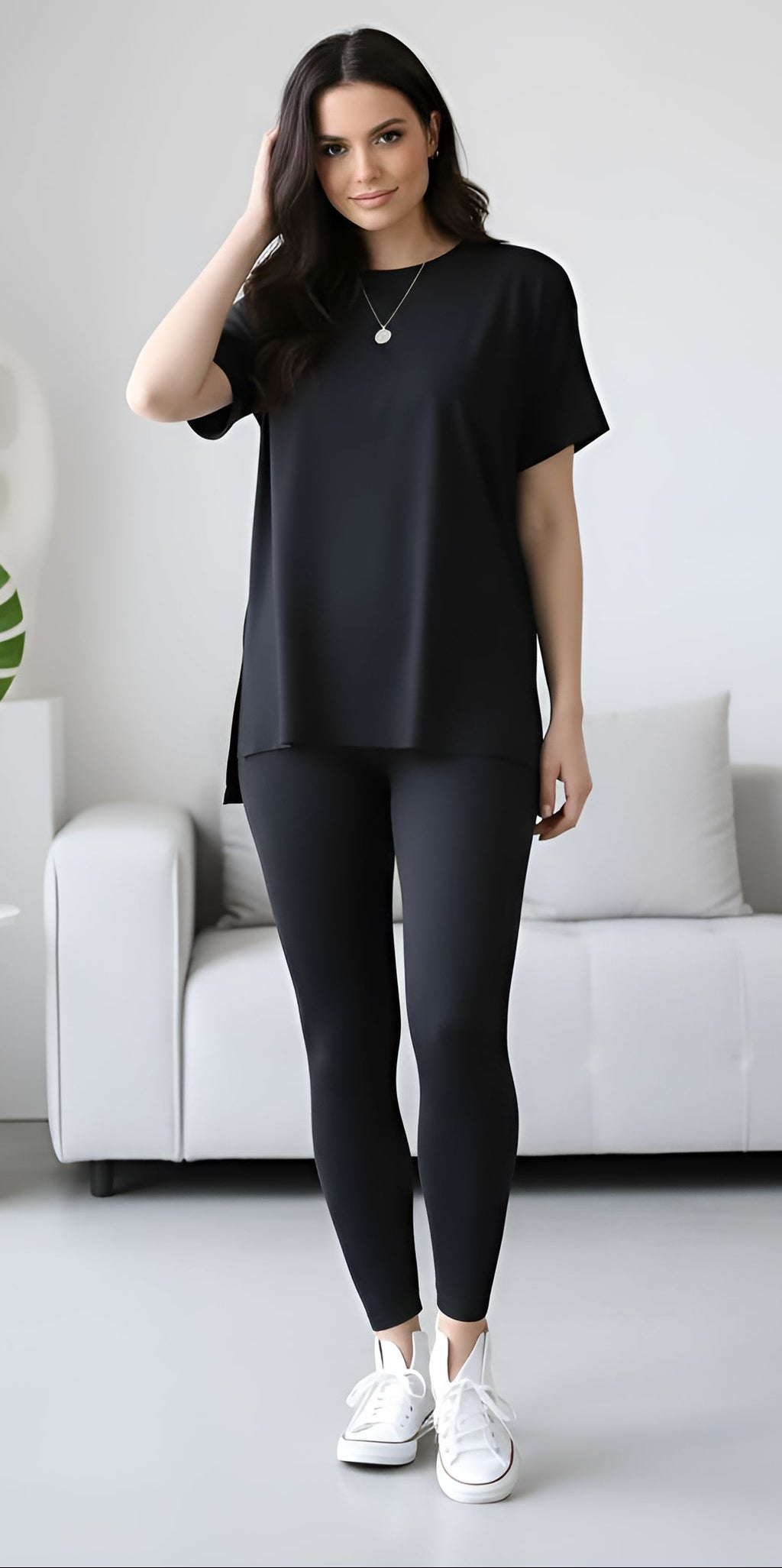 Woman wearing a black outfit in a minimalistic room with a white sofa and decorative items.