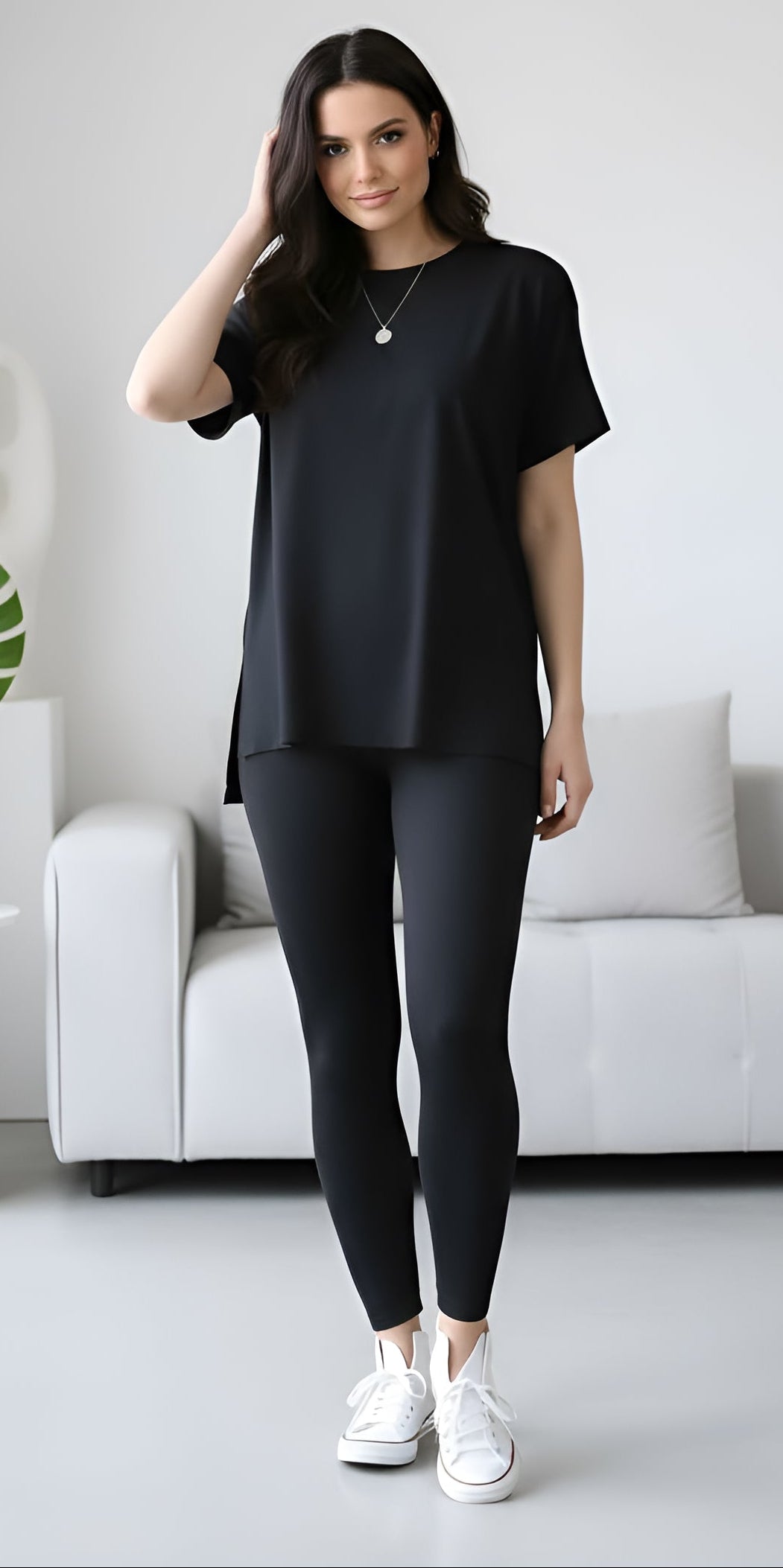 Woman wearing a black outfit in a minimalistic room with a white sofa and decorative items.