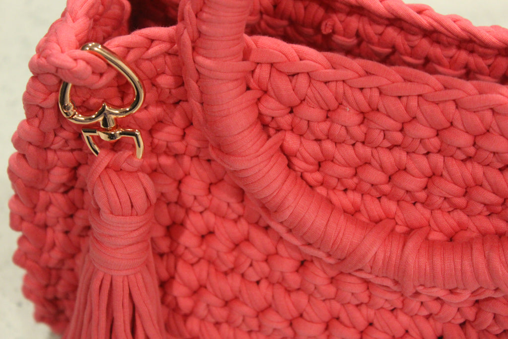 Close-up of a pink textured handbag with a gold heartshaped clasp and tassel.