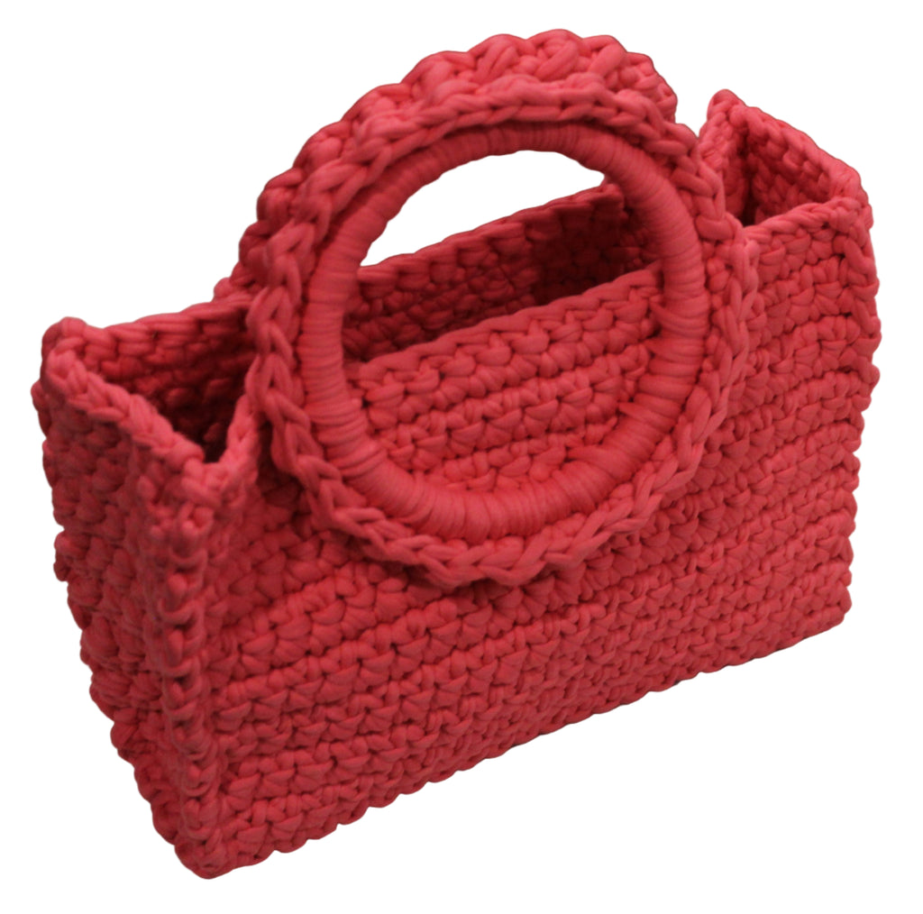 coral pink hand knitted handbag on a white surface with a vintage radio in the background