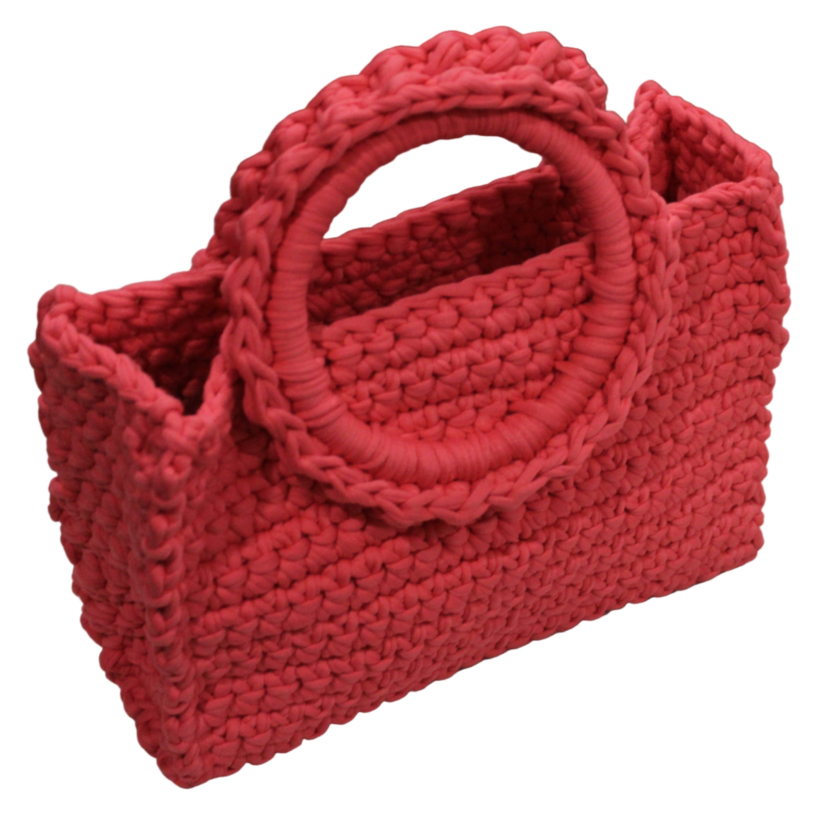 coral pink hand knitted handbag on a white surface with a vintage radio in the background