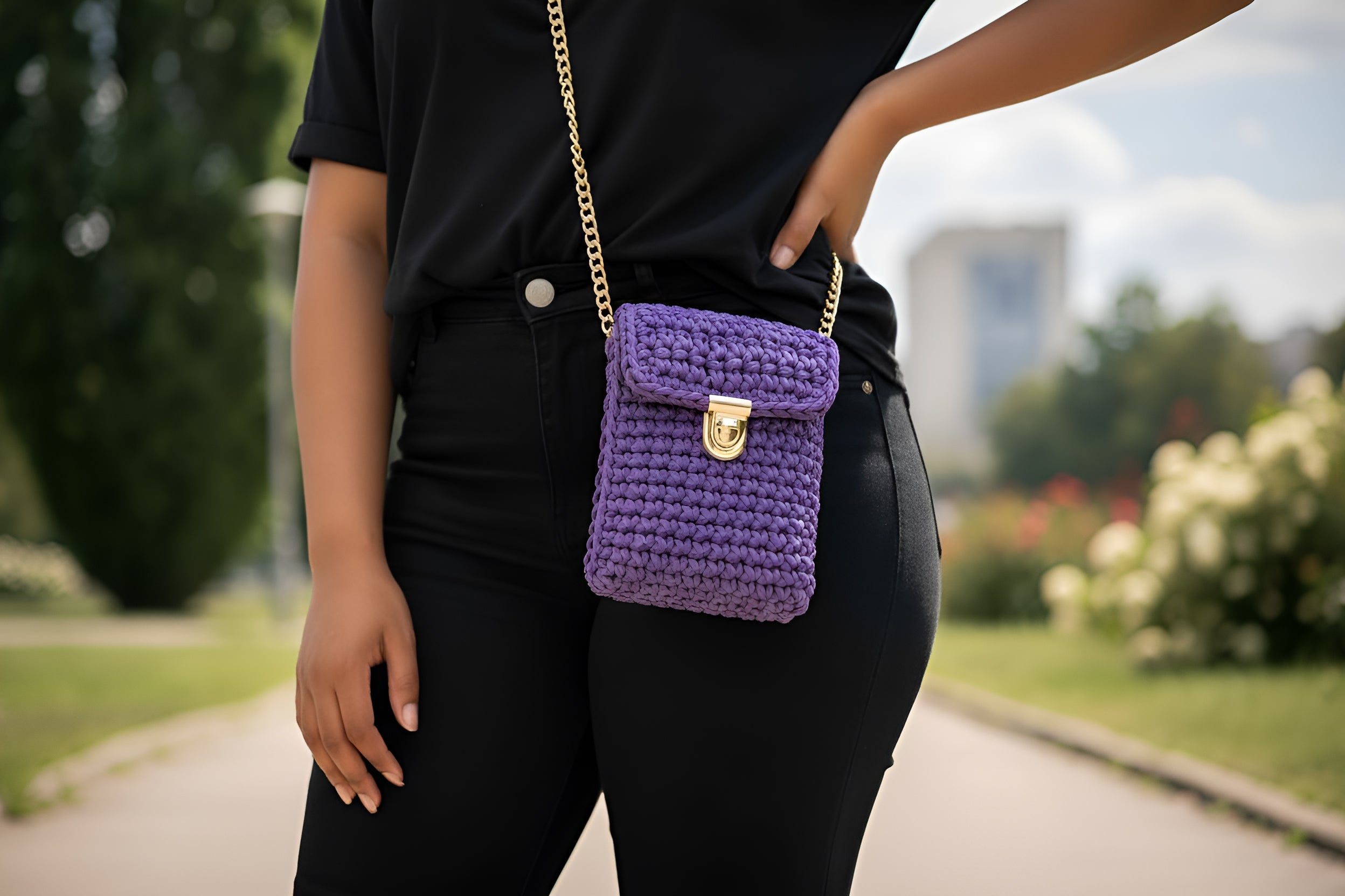 Person wearing a black outfit with a purple hand knitted crocheted bag in an outdoor setting