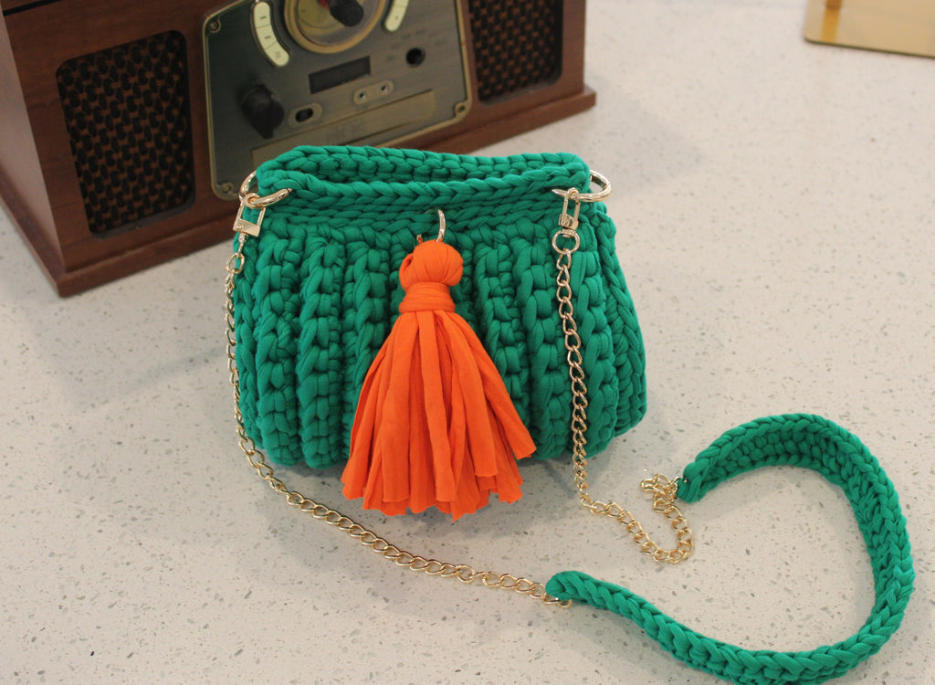 Green hand knitted handbag with an orange tassel on a light surface